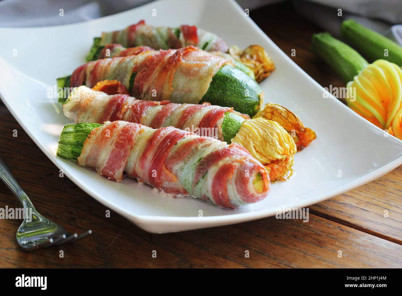 Des courgettes grillées emballées dans un bacon sur une assiette blanche. Banque D'Images