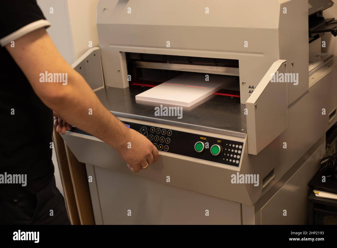 Image rognée mains de l'homme à l'aide d'une machine à couper le papier, guillotine, décalage. Boutons, carte électronique, affichage, réglage du niveau du laser Banque D'Images