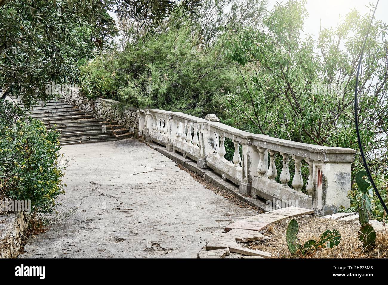 Escalier en pierre et balcon avec balustrade près du jardin. Branches d'arbres penchées sur les escaliers et sol en béton à la lumière du soleil Banque D'Images