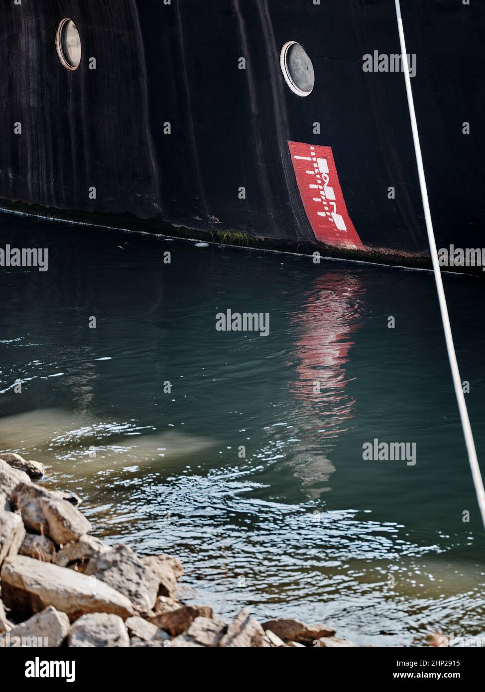 Marquage rouge à l'échelle de tirant d'eau sur la coque noire d'un cargo reflété dans l'eau du port. Banque D'Images
