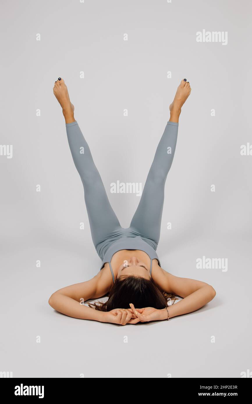 Femme fait du sport. Brunette fait de l'exercice de yoga ou de fitness, elle est allongée sur le dos avec ses jambes en haut et ses mains sont derrière sa tête Banque D'Images