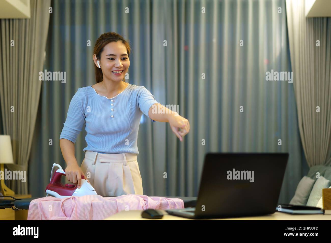 Femme asiatique travaillant à la maison effectuant des travaux ménagers repassage dans le salon de la maison et vidéoconférence en ligne avec des collègues sur ordinateur portable Banque D'Images