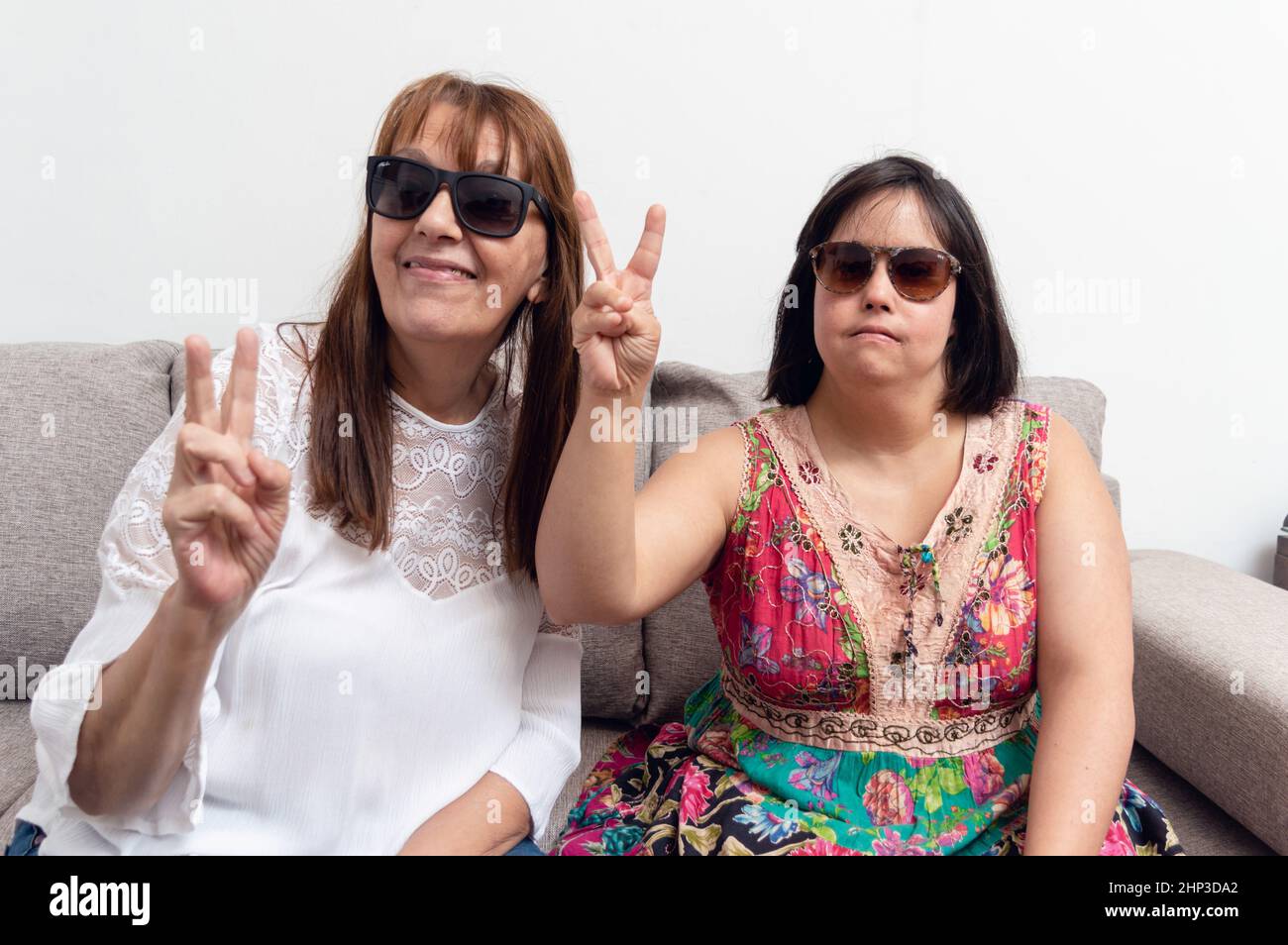 Portrait de deux femmes caucasiennes adultes latines faisant le V signe, la mère et la fille faisant la paix et l'amour signe regardant la caméra, les personnes handicapées concept. Banque D'Images