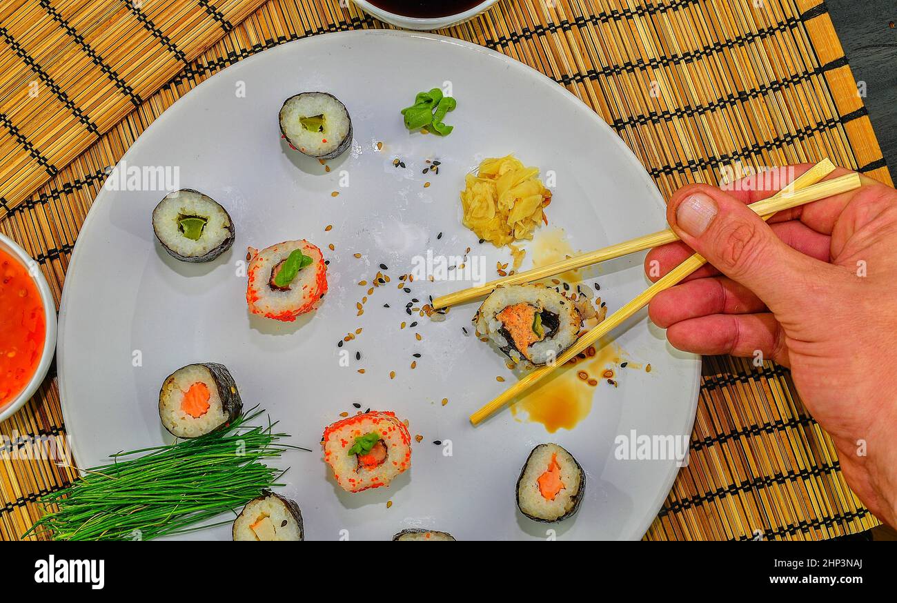 Rouleau de manger des sushis dans un restaurant japonais, part avec des baguettes fermer -haut. La main d'un homme tenant les sushi avec des baguettes. Banque D'Images