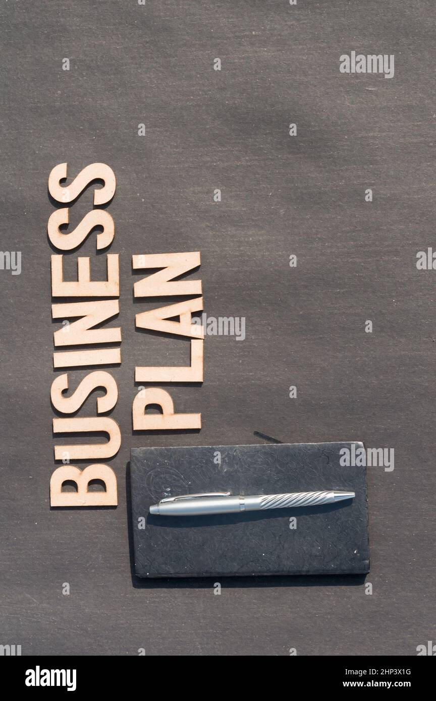 Main d'homme d'affaires plaçant un stylo et un carnet devant le plan d'affaires Word fait de blocs de bois de lettres Alphabet.Vue grand angle.Rétrogr. Vertical Banque D'Images