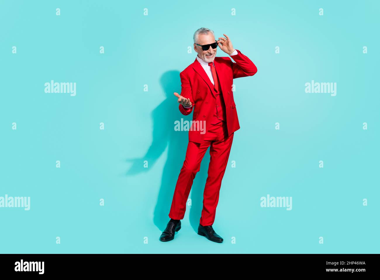 Photo de funky retraité homme porter un costume rouge lunettes sombres vous invitant à danser isolé couleur turquoise arrière-plan Banque D'Images