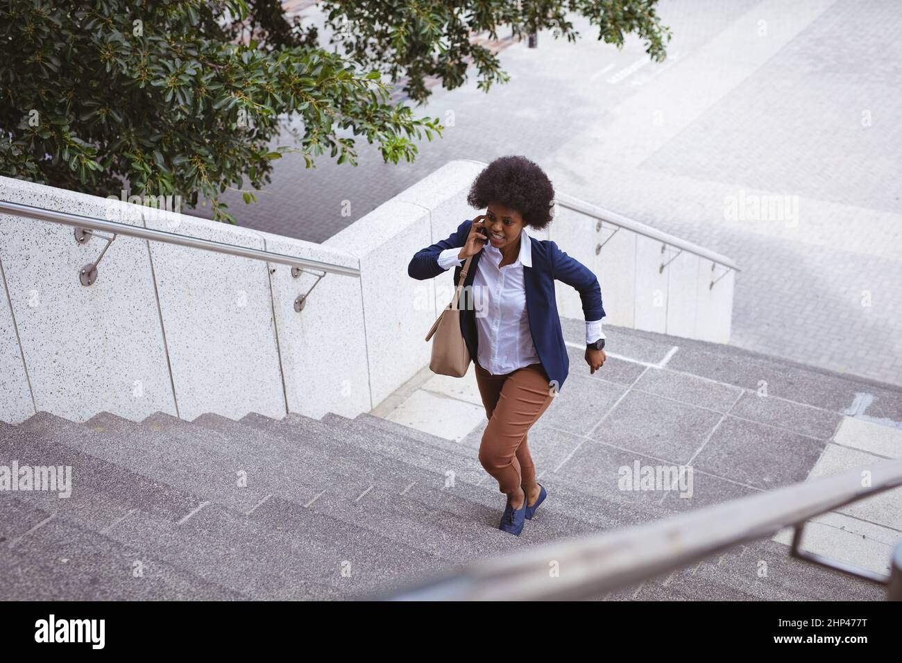 Femme d'affaires afro-américaine de taille moyenne, qui parle au téléphone tout en se précipitant dans la ville Banque D'Images