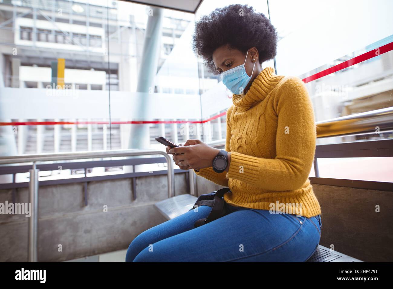 Femme d'affaires afro-américaine de taille moyenne, portant un masque avec un smartphone lorsqu'elle est assise à l'aéroport Banque D'Images