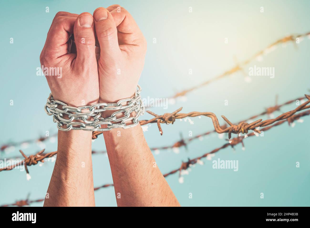Les mains attachées avec une chaîne métallique soulevée contre la clôture en fil barbelé.Emprisonnement, esclavage, droits de l'homme, liberté. Banque D'Images