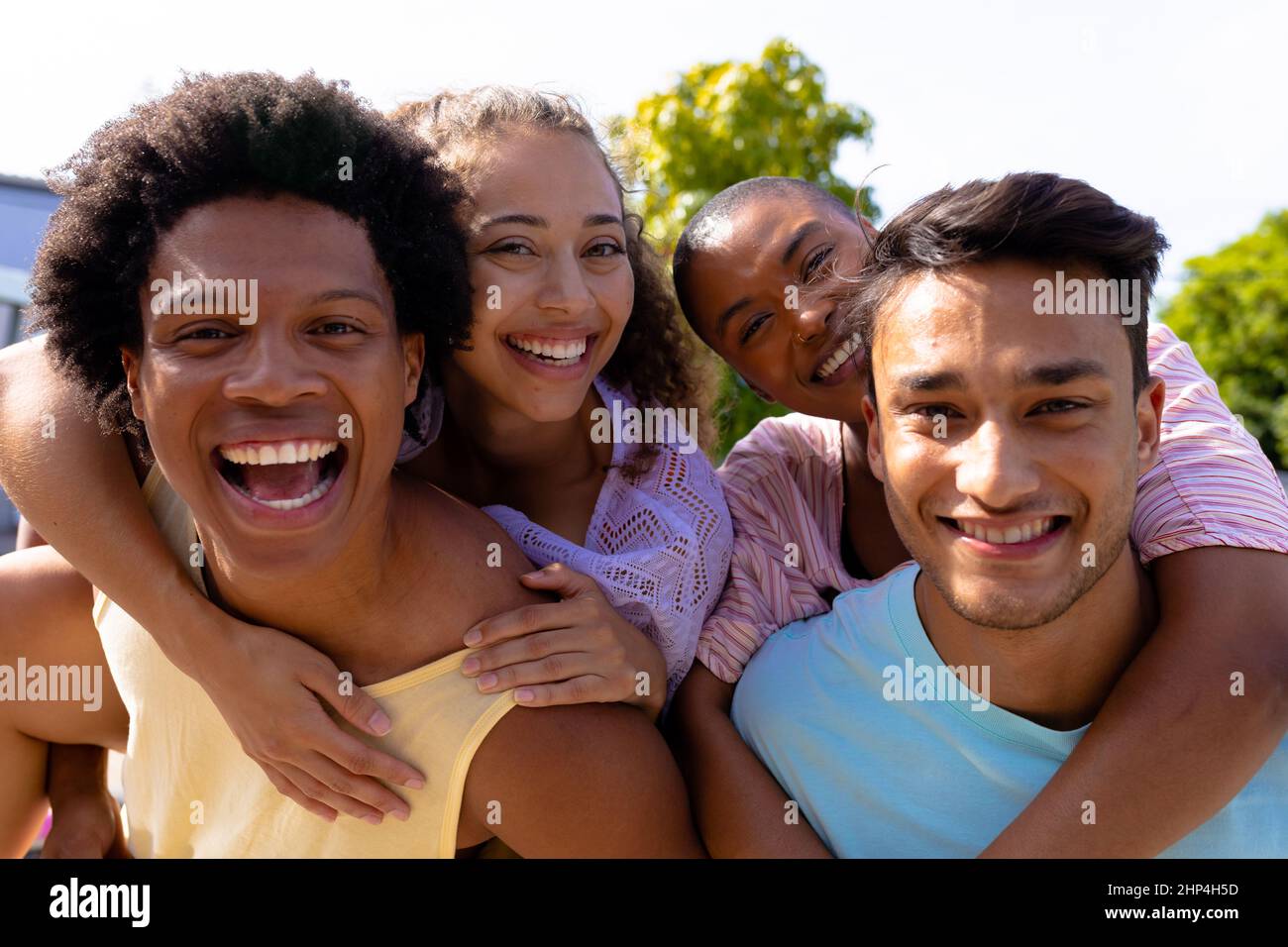Portrait d'hommes multiraciaux souriants offrant des promenades en porcgyback aux femmes par temps ensoleillé Banque D'Images