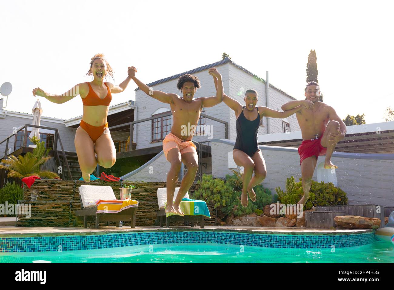 Portrait complet de jeunes enthousiastes multiraciaux hommes et femmes tenant les mains sauter dans la piscine Banque D'Images