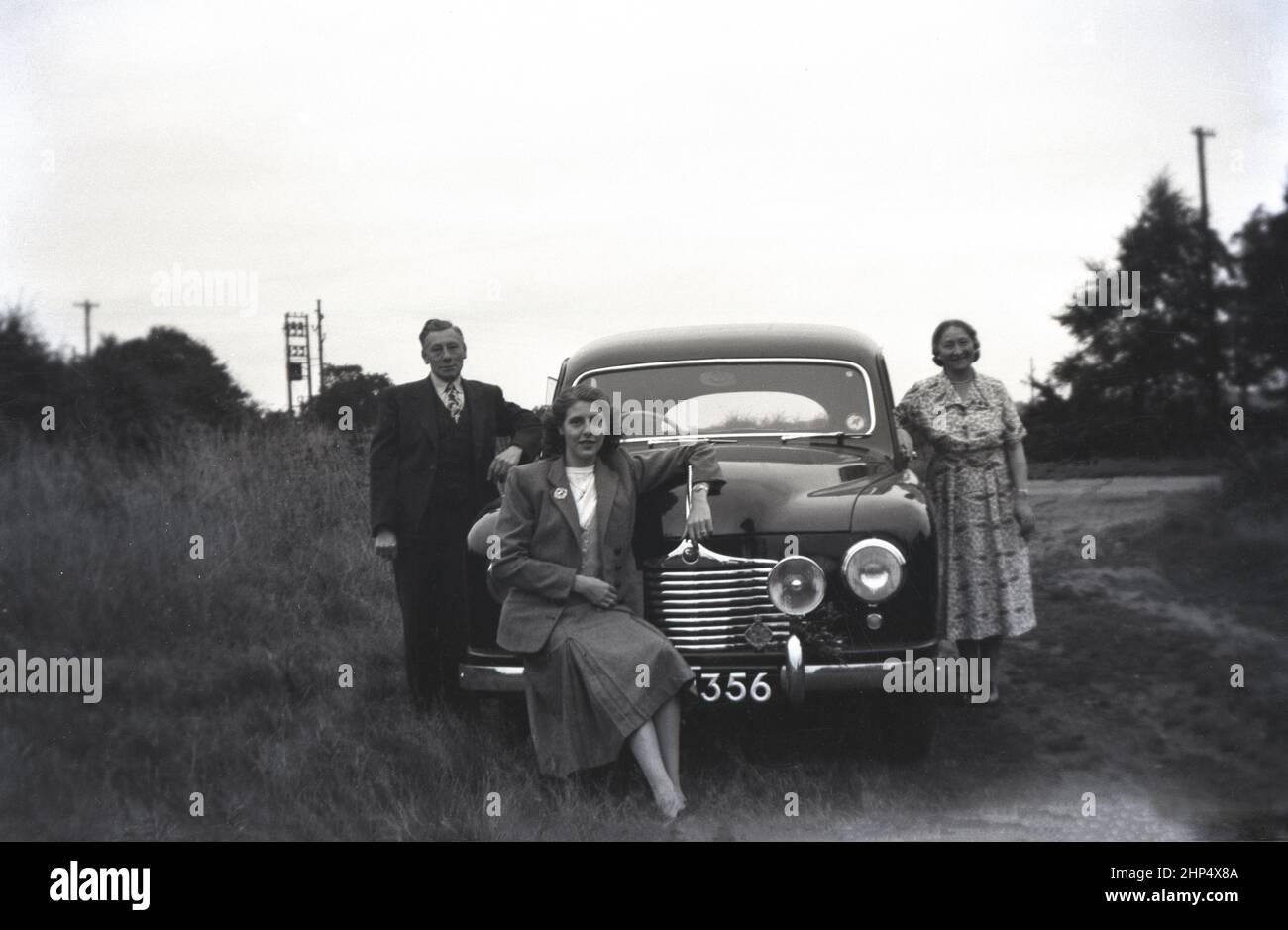 1949, historique, à l'extérieur sur une piste de comté boueuse, un père, une mère et une fille posant par leur nouvelle voiture, un chanteur SM1500, Angleterre, Royaume-Uni. Petite berline familiale de 4 portes produite entre 1948 et 1956, la SM1500 a été fabriquée par Singer Motors, une entreprise automobile britannique fondée en 1874 à Coventry, en Angleterre, par George Singer. D'origine fabricant de bicyclettes, en 1901, l'entreprise a commencé à fabriquer des voitures à moteur. Banque D'Images