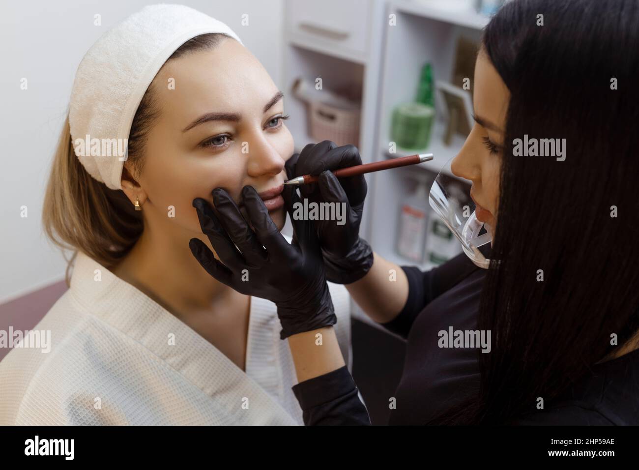 Jeune femme avec maquillage permanent sur ses lèvres dans un salon de cosmétologues. Maquillage permanent (tatouage) dessiner une ligne avec un crayon rouge à lèvres Banque D'Images