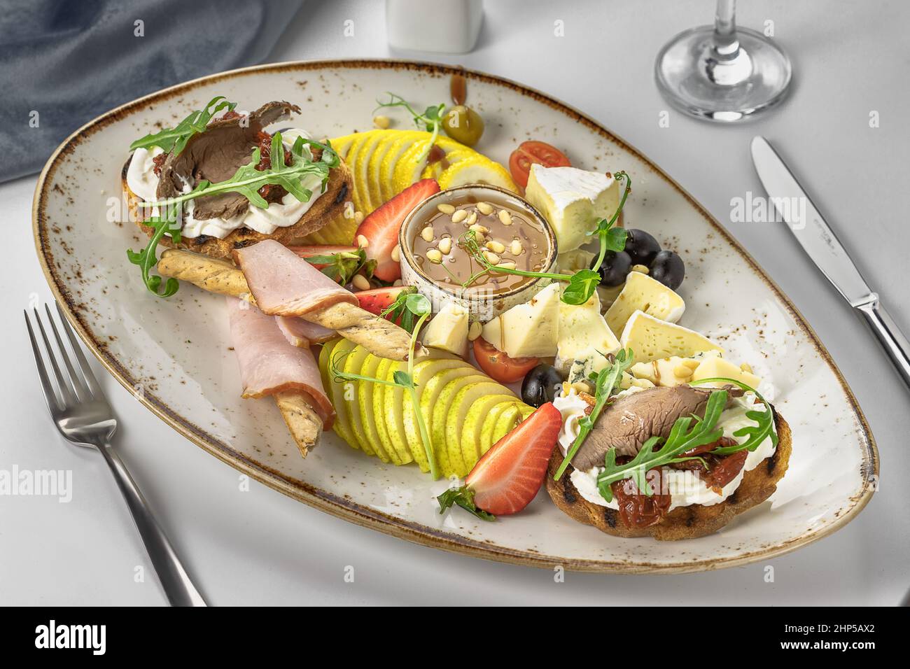 plat de banquet avec poires en tranches, fromages et tomates, avec bruschettas au rôti de boeuf, sauce à la crème, tomates séchées et arugula, avec bâtonnets de pain Banque D'Images