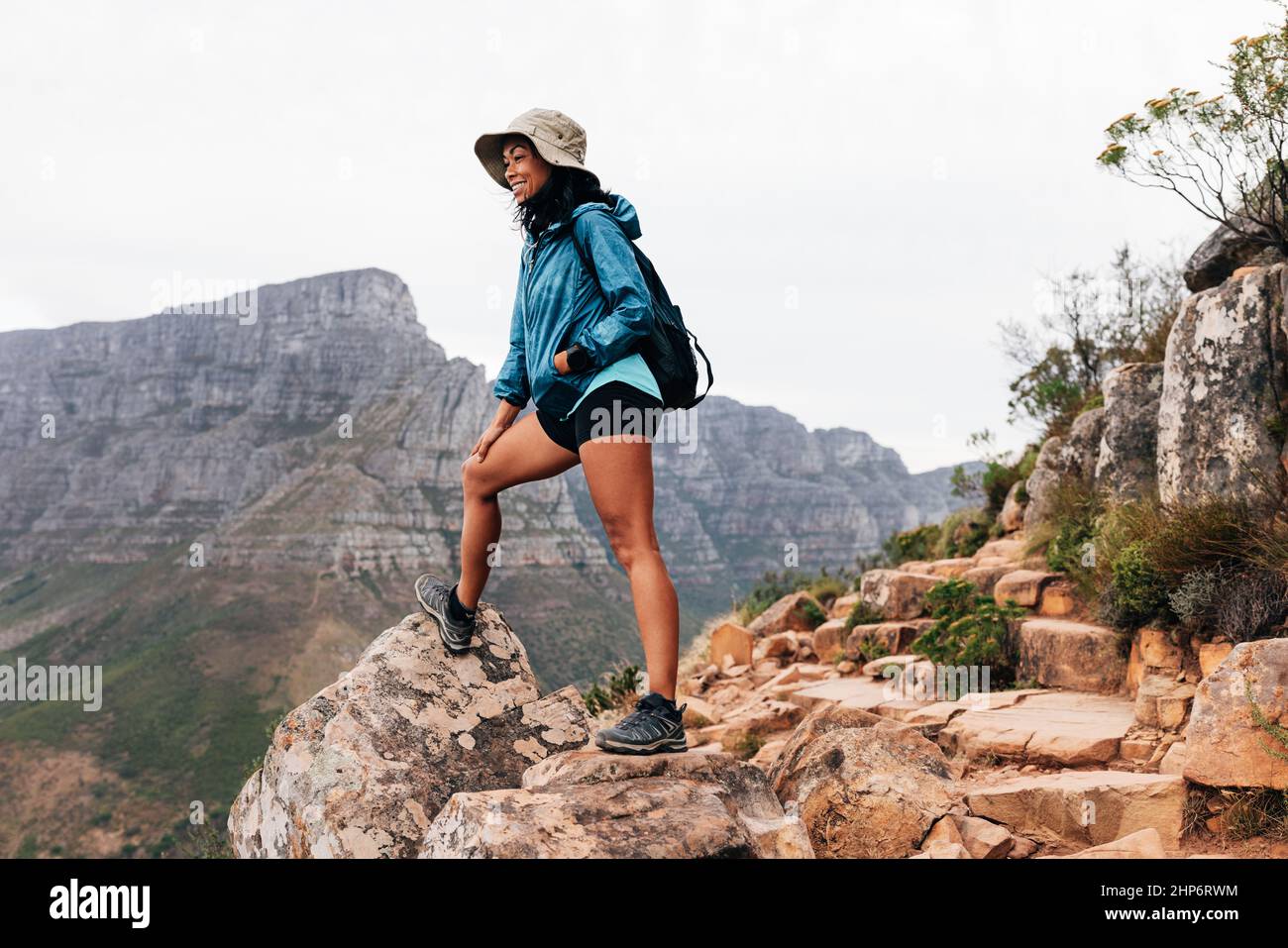 Femme portant un chapeau et des vêtements de sport se détendant pendant une  randonnée en montagne. Femme souriante qui regarde vers le bas en se tenant  sur un bord Photo Stock -