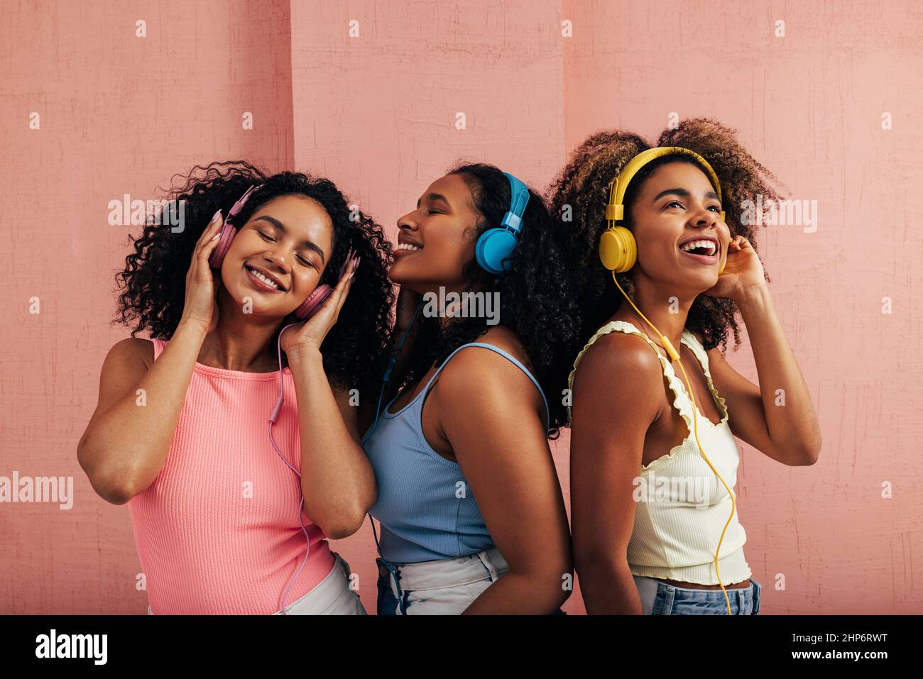 Trois belles femmes debout ensemble et à l'écoute de la musique. Des amies avec casque portant des vêtements décontractés et lumineux pour une bonne humeur et de la musique Banque D'Images