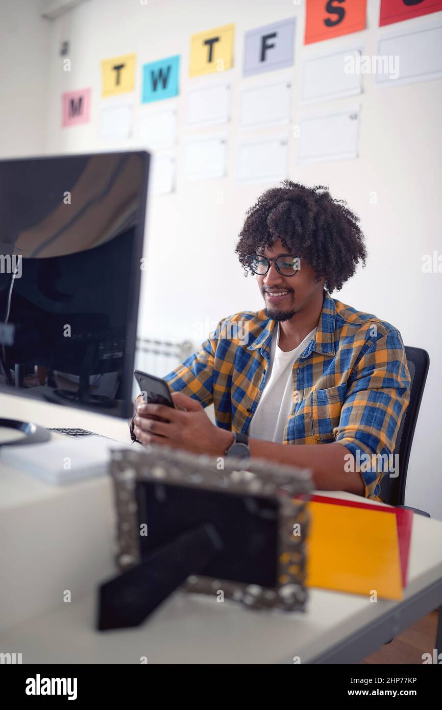 Un jeune homme assis au bureau dans une atmosphère agréable au bureau et envoyant des SMS sur le smartphone. Employés, travail, bureau Banque D'Images