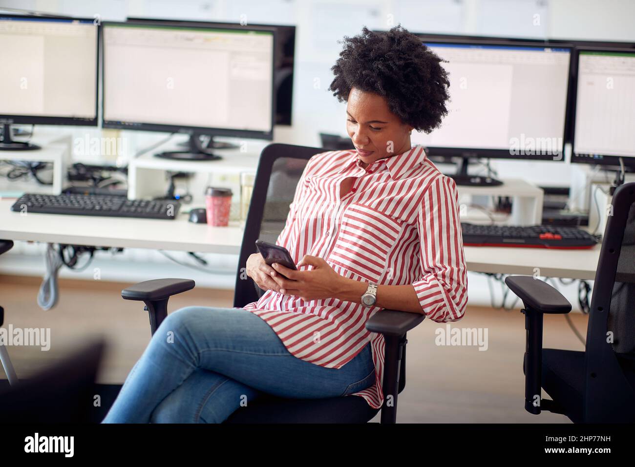 Une jeune femme s'asseyant au bureau dans une atmosphère agréable au bureau et envoyant des SMS sur le smartphone. Employés, travail, bureau Banque D'Images