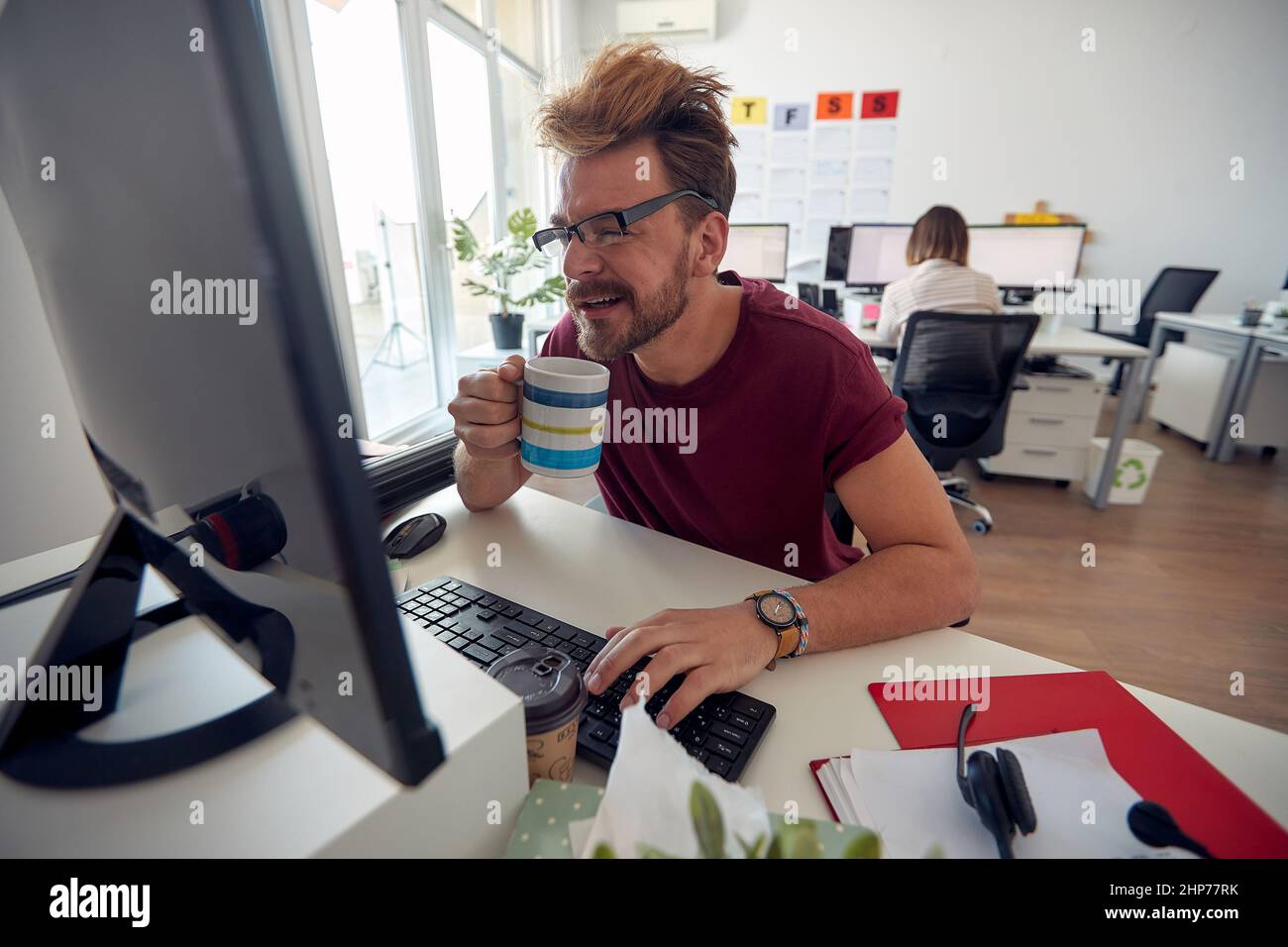 Un jeune employé de sexe masculin boit un café tout en travaillant dans une atmosphère uniforme au bureau. Employés, travail, bureau Banque D'Images