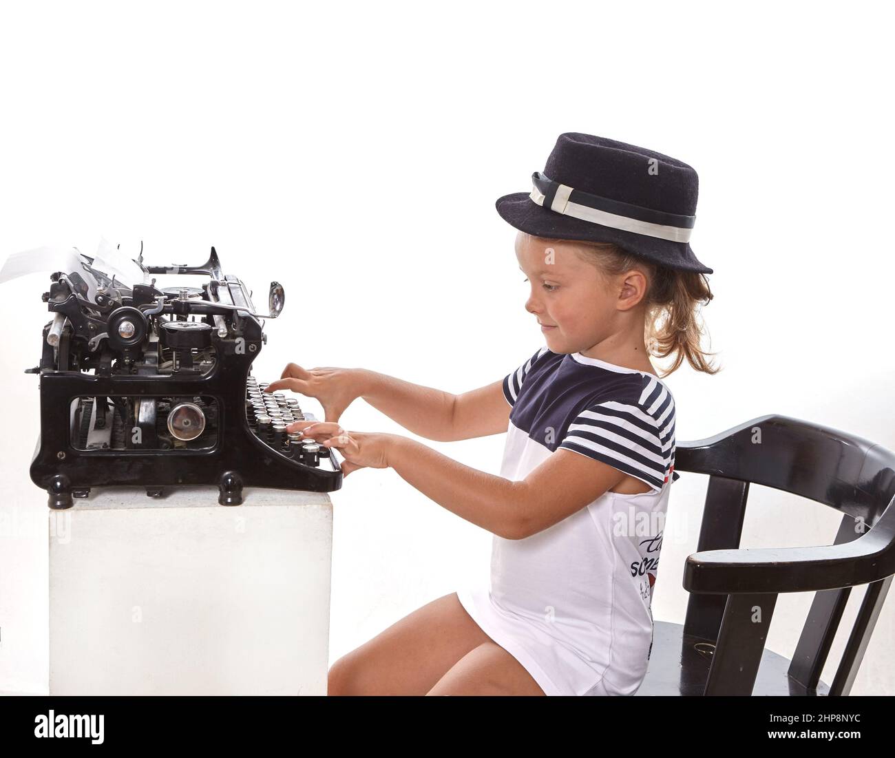 Jolie petite fille en chapeau dactylographiant sur une machine à écrire antique sur fond blanc. Concept d'éducation.fcool Banque D'Images