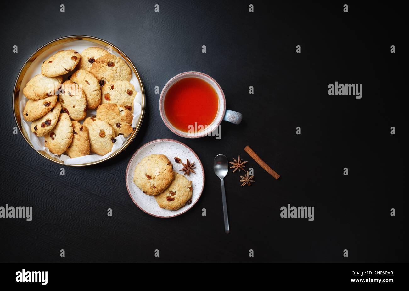 Petits gâteaux faits maison aux flocons d'avoine, tasse de thé, cuillère, bâton de cannelle et anis étoilé sur table noire. Copier l'espace pour le texte. Pose à plat. Banque D'Images