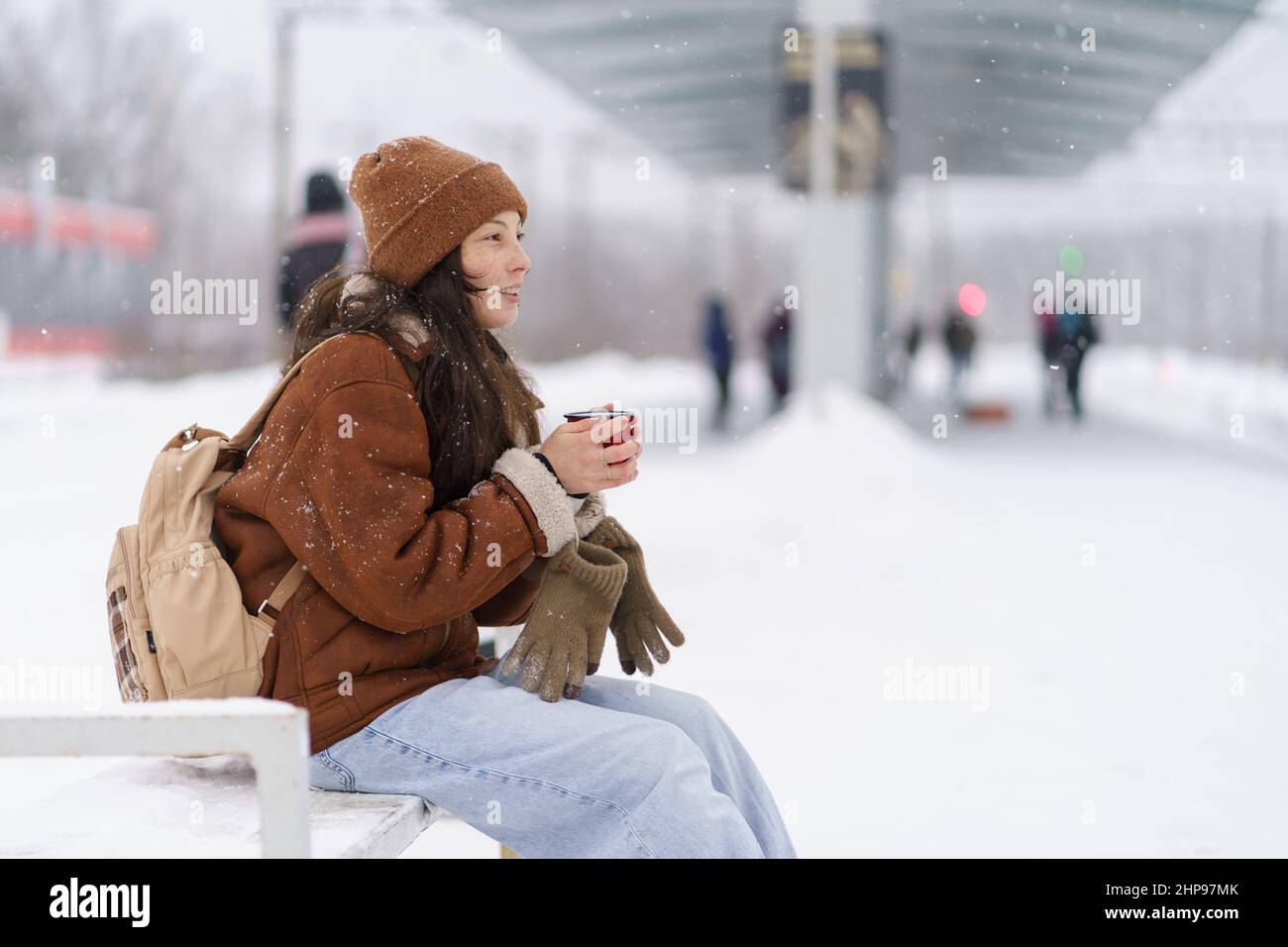 Femme voyageur fatiguée mais heureuse avec une tasse de thé chaud attendant que le train arrive en hiver Banque D'Images