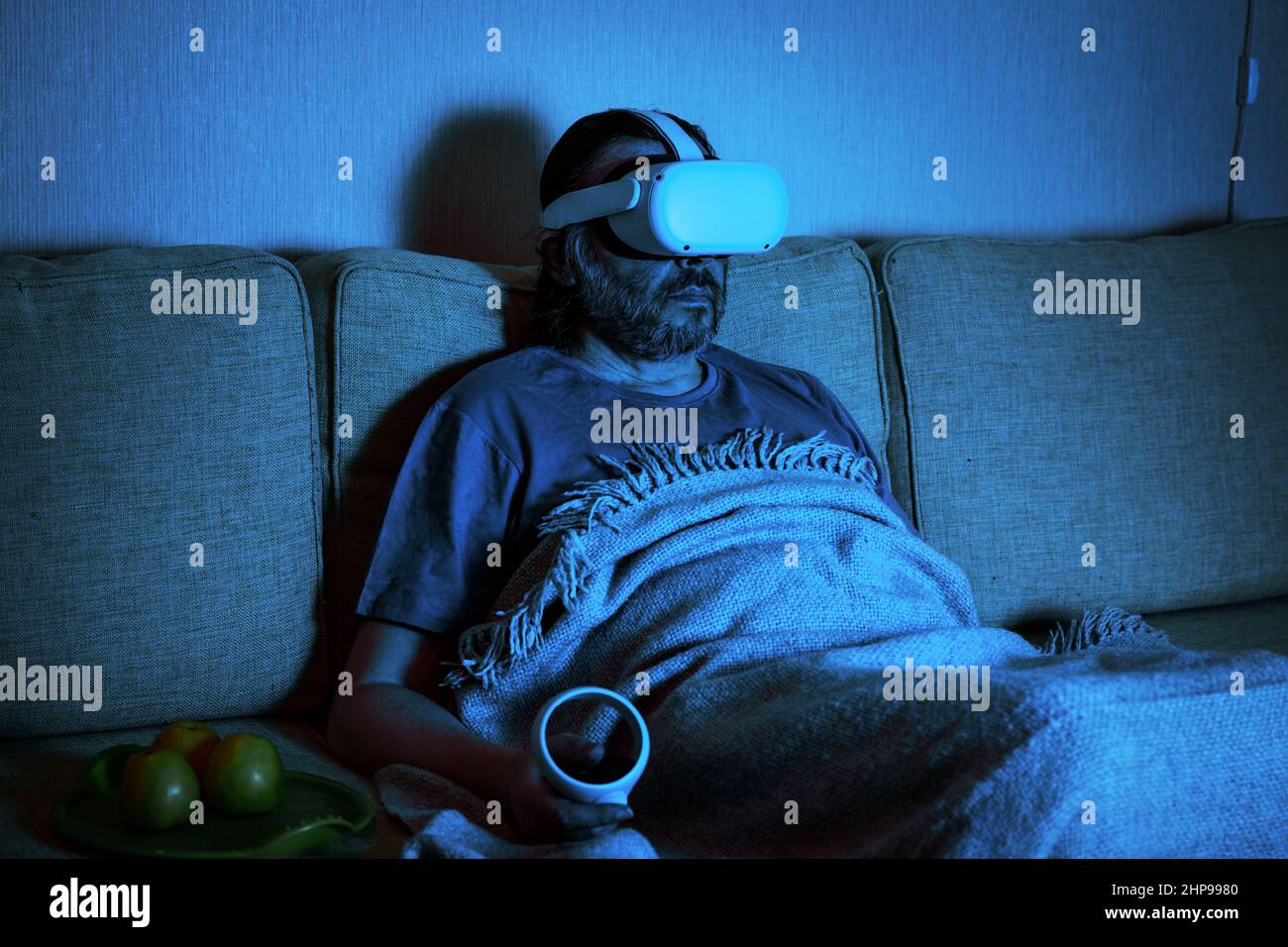 Homme utilisant un casque de réalité virtuelle regarde la télévision ou le film dans l'obscurité, personne assise sur le canapé regarde dans des lunettes VR. Concept de jeux vidéo, futuriste Banque D'Images