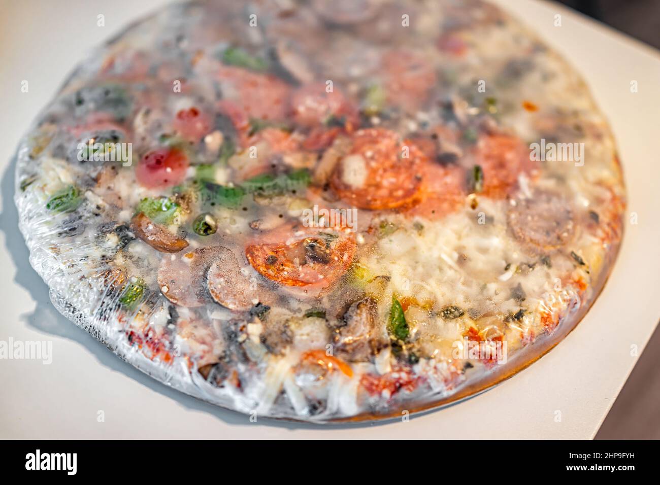 Pizza suprêmes toute entière congelée avec une croûte mince de plastique enveloppée sur la table avec des saupoudrés de fromage mozzarella et de la sauce tomate rouge, des tranches de pepperoni et Banque D'Images