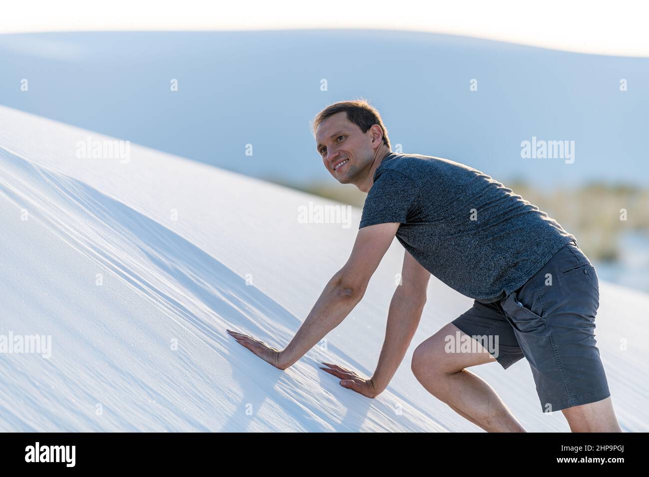 Joyeux jeune homme souriant grimpant sur tous les fours sur une colline de sable dans les dunes de sable blanc monument national au Nouveau-Mexique à un doux coucher de soleil Banque D'Images