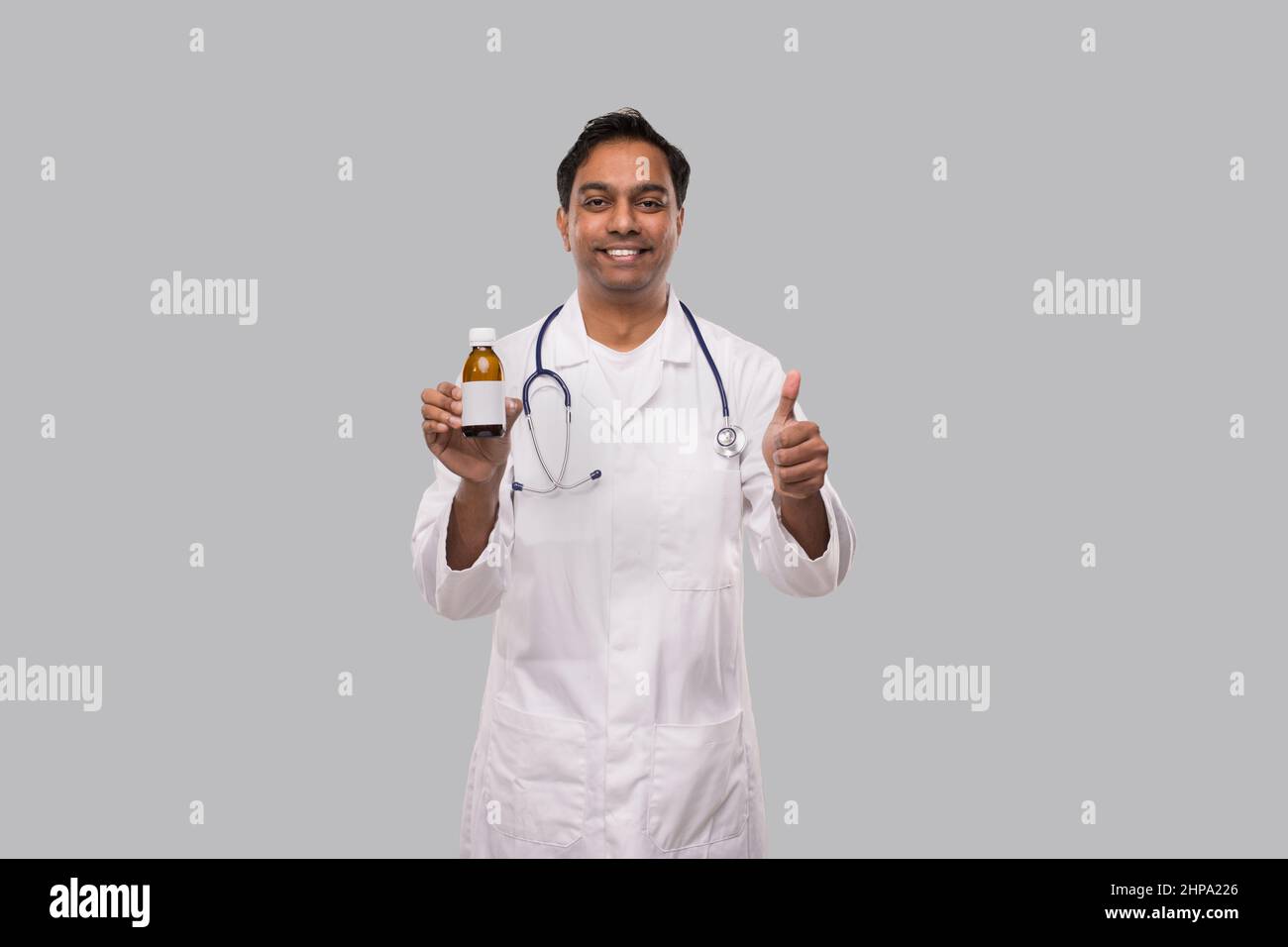 Indian Man Doctor tenant le sirop contre la toux montrant Thumb Up isolé Banque D'Images