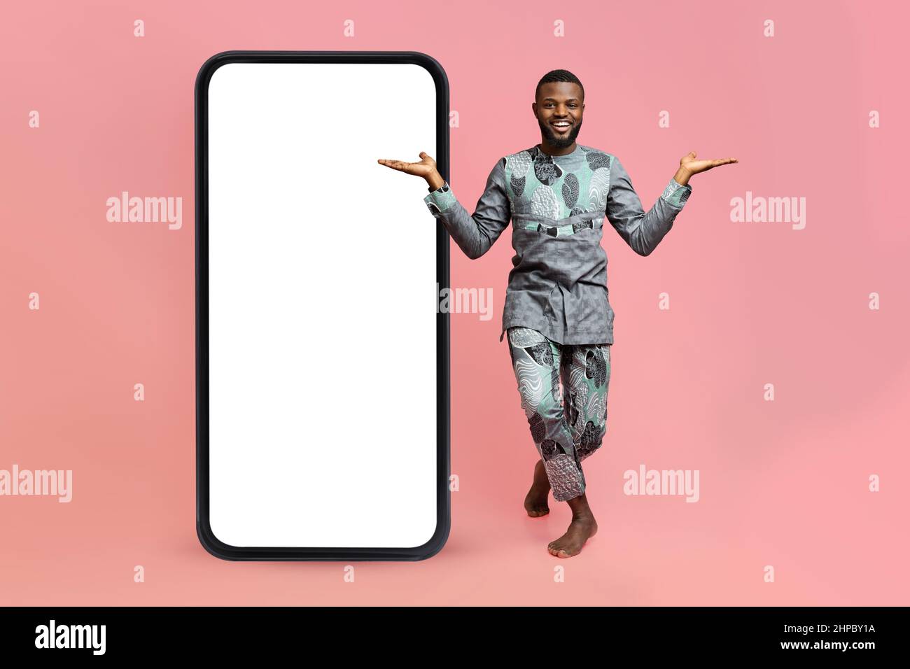 Homme afro-américain en costume traditionnel dansant près d'un grand smartphone vierge, démontrant l'espace de copie pour la publicité Banque D'Images