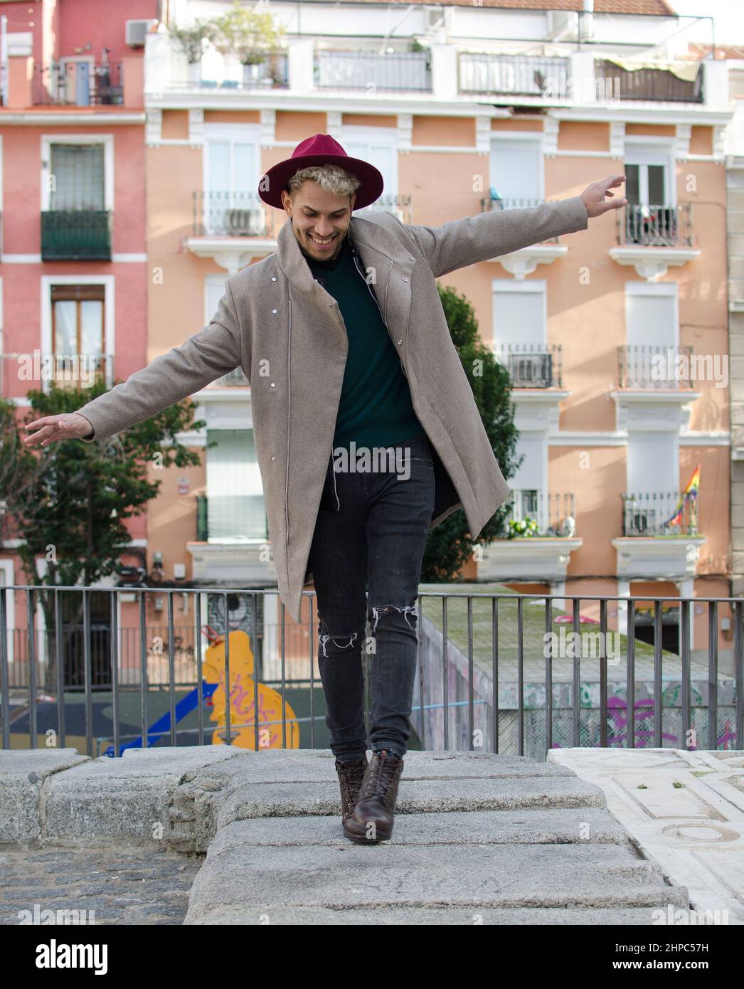 Jeune modèle tendance avec veste grise et chapeau rouge faisant l'équilibre drôle dans la rue Banque D'Images