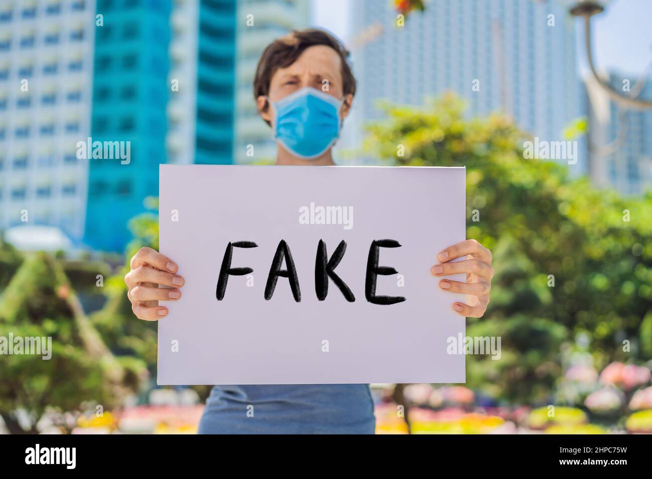 L'homme dans le masque médical prévient la maladie du coronavirus tient une fausse affiche. Texte écrit à la main - lettrage isolé sur blanc. Coronovirus COVID 19 concept Banque D'Images