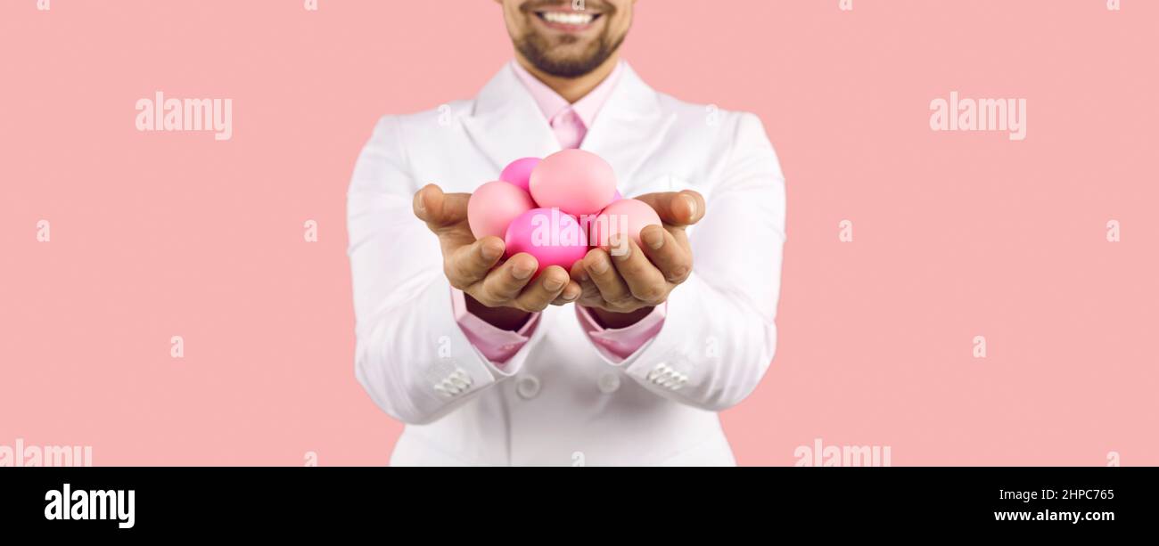 Bannière avec une coupe courte d'un homme heureux souriant et tenant une poignée d'oeufs de Pâques roses Banque D'Images