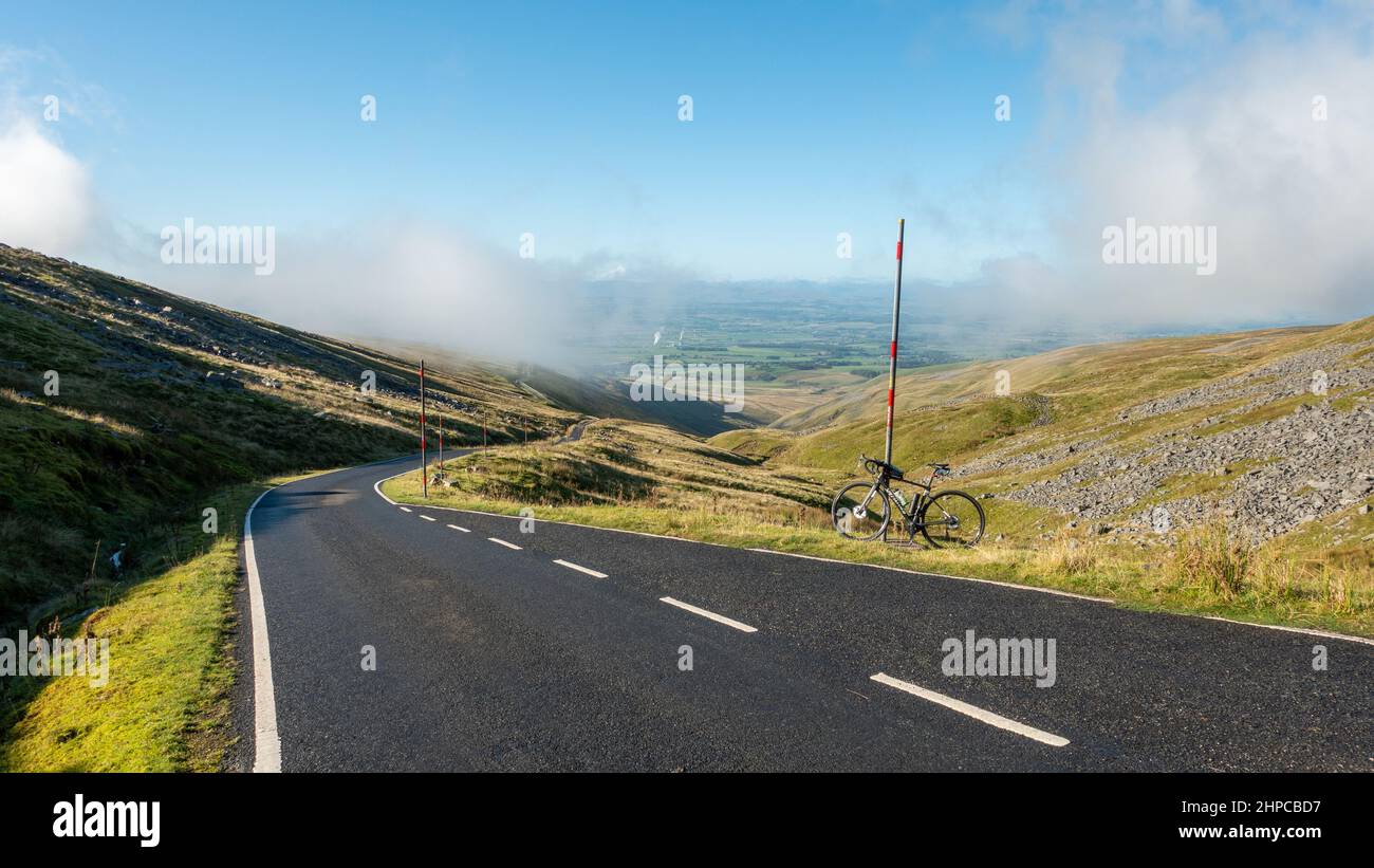Célèbre randonnée cycliste sur la route à sens unique de Great Dun est tombé dans la vallée de l'Eden avec le vélo de route adossé contre la neige pole, Cumbria, Angleterre, Royaume-Uni Banque D'Images