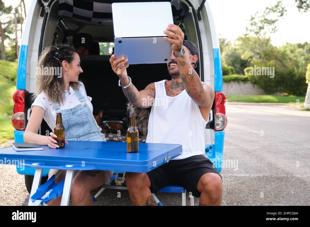 Un jeune couple tatoué sourit et parle lors d'un appel vidéo sur ordinateur portable pendant un voyage en minibus. Banque D'Images