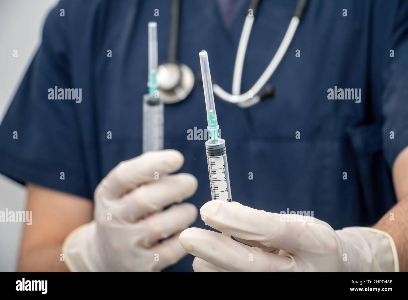 Médecin en uniforme médical tient, à la main avec un gant jetable, seringue vide. Estomper le médecin avec la seringue et le stéthoscope autour de son arrière-plan de cou. Banque D'Images