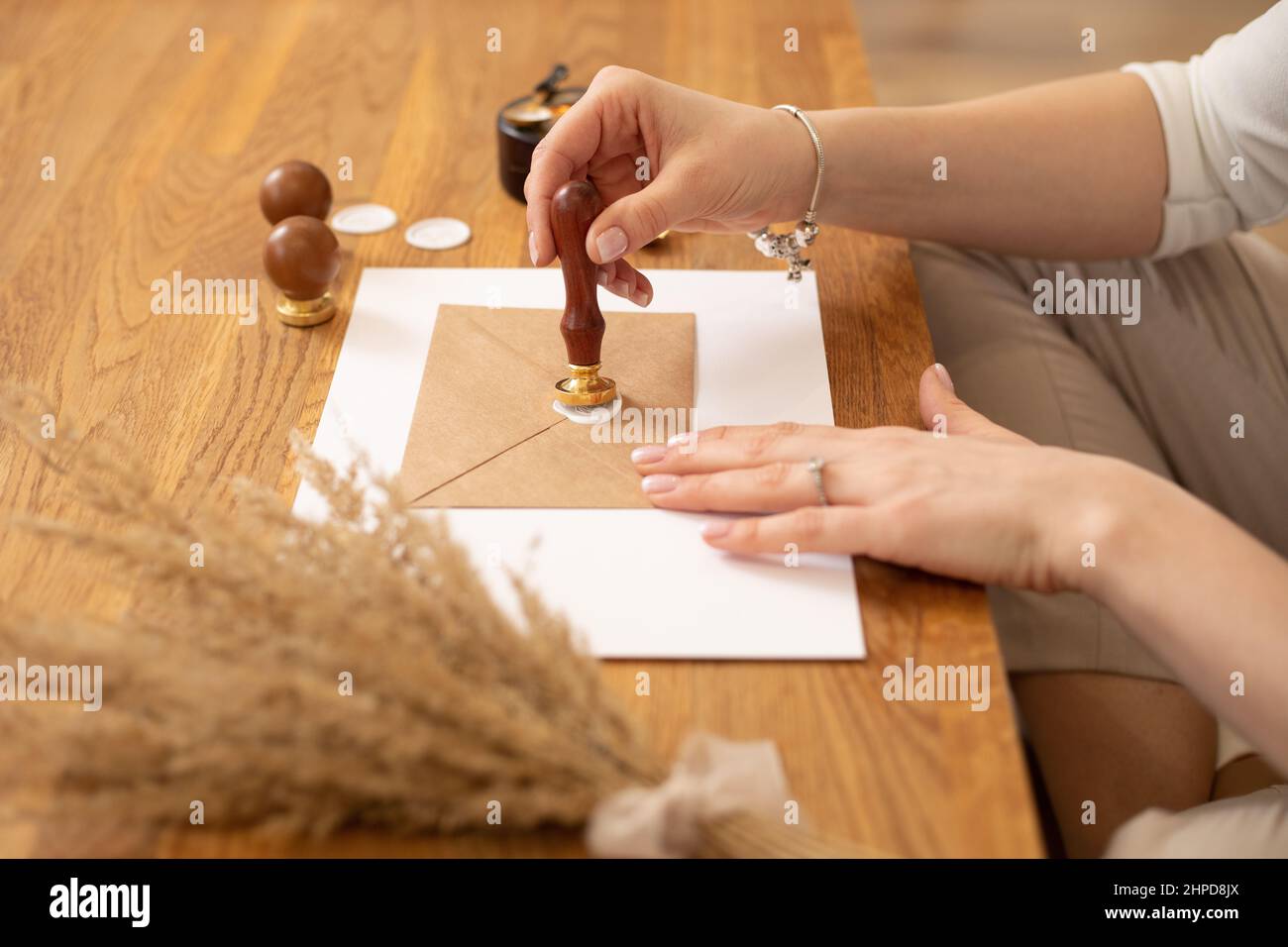Photo courte des mains de femme faisant le désherbage invitation enveloppe artisanat, assis à un bureau en bois, mettant l'impression de cire d'étanchéité. Banque D'Images