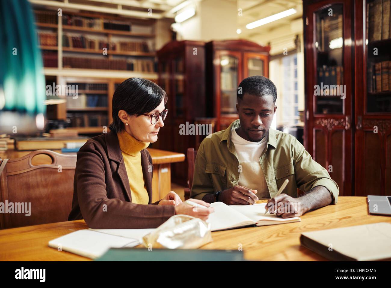 Portrait d'une femme mature professeur tutorat afro-américain étudiant en intérieur de bibliothèque classique à l'université Banque D'Images