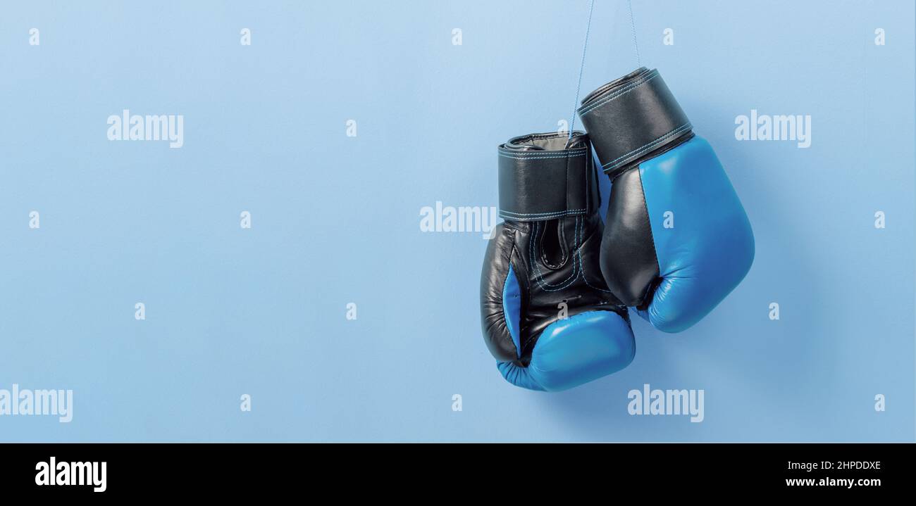 Des gants de boxe bleus sont suspendus sur un mur bleu. Modèle espace de copie pour le texte. Maquette. Banque D'Images