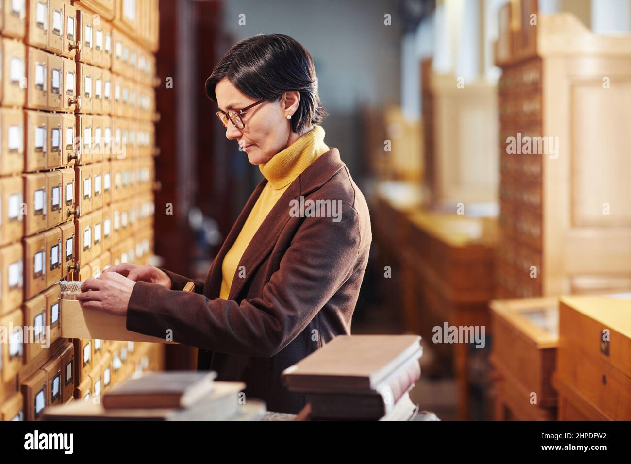 Vue latérale d'un bibliothécaire féminin recherchant un livre dans l'armoire du catalogue de la bibliothèque Banque D'Images