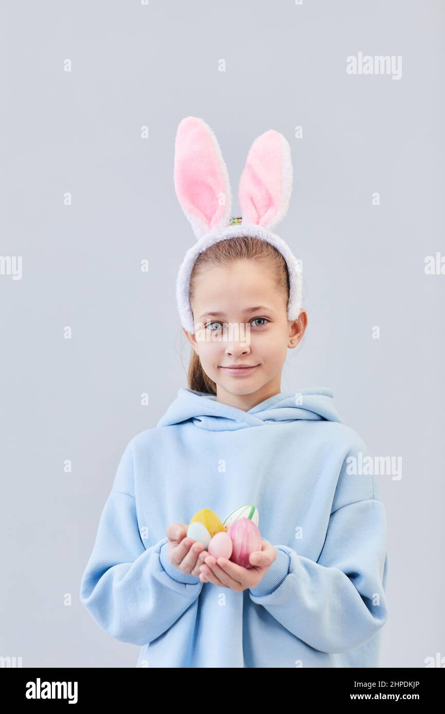 Portrait vertical d'une jeune fille adorable portant des oreilles de lapin et tenant des œufs de Pâques sur fond blanc, espace de copie Banque D'Images