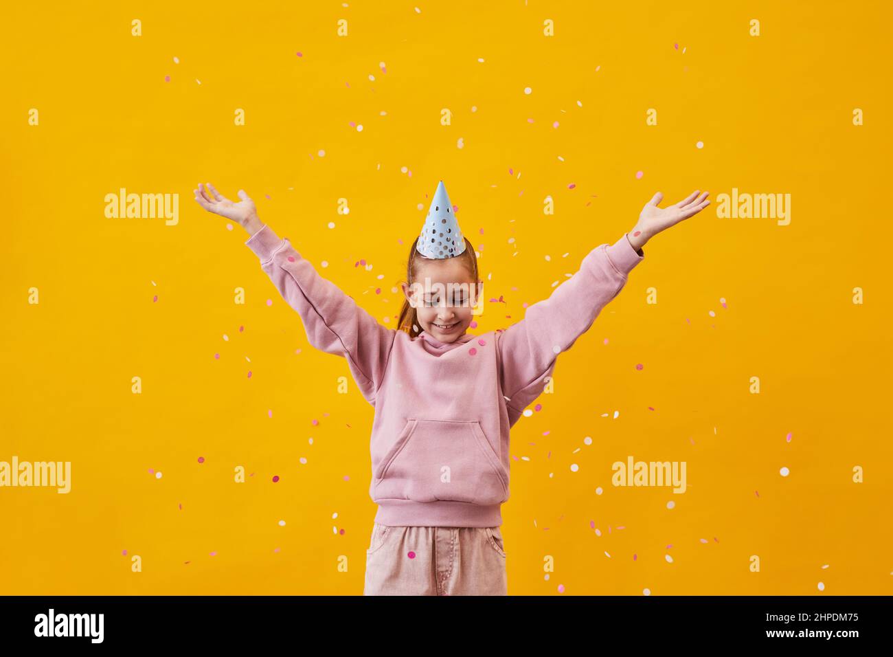 Portrait pop de la jeune fille adolescente dansant dans des confetti sur fond jaune vif, espace de copie Banque D'Images