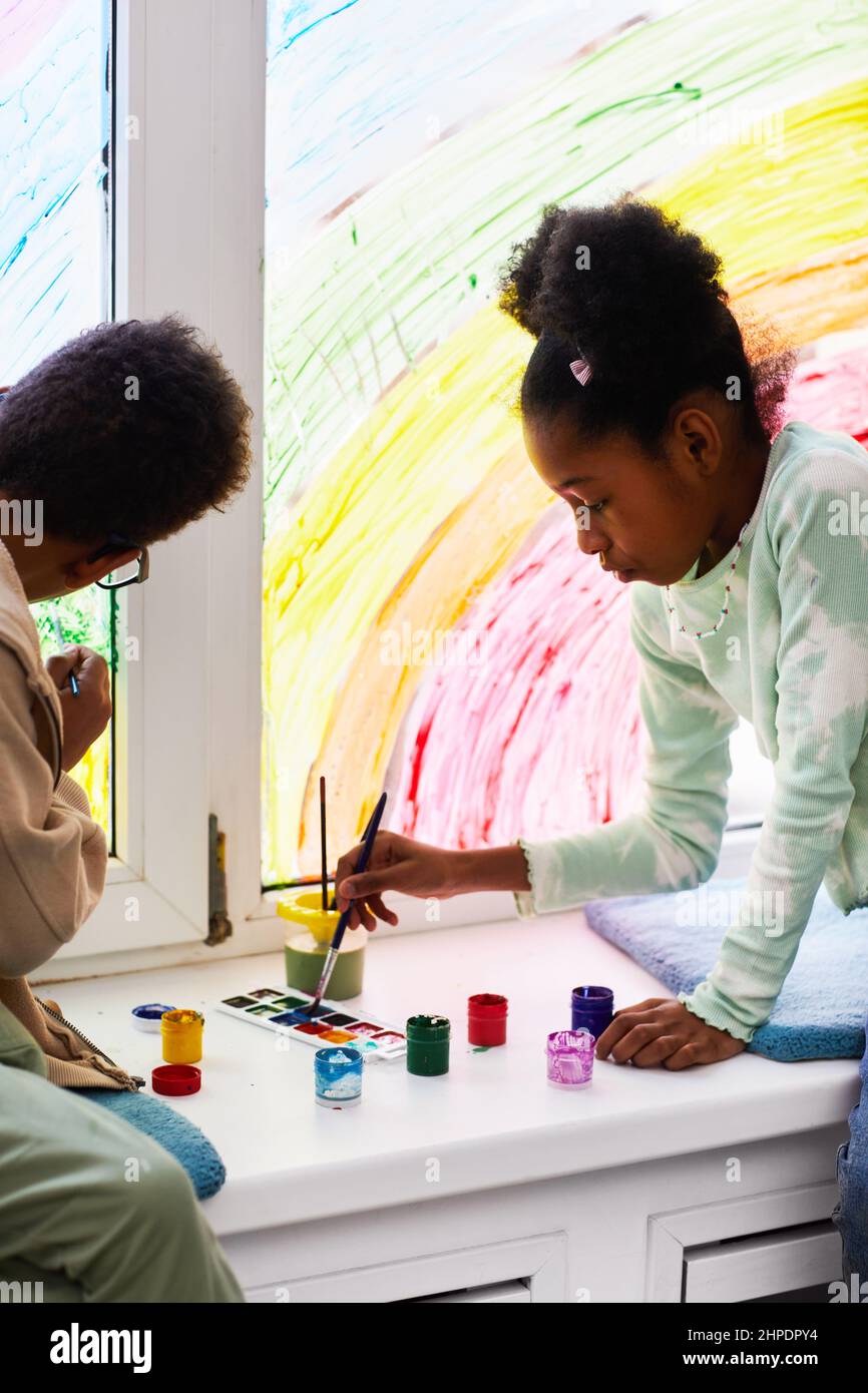 Portrait vertical de deux enfants afro-américains dessinant avec de la peinture sur les fenêtres tout en décorant la chambre des enfants ensemble Banque D'Images