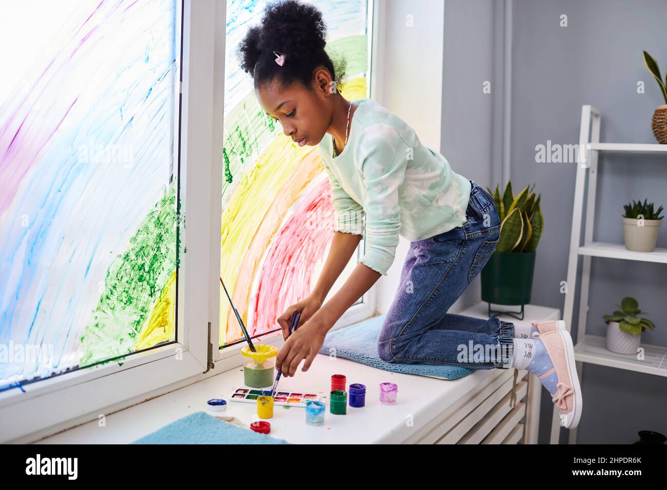 Portrait en longueur de fille afro-américaine dessin avec de la peinture sur les fenêtres tout en décorant la chambre des enfants, copier l'espace Banque D'Images