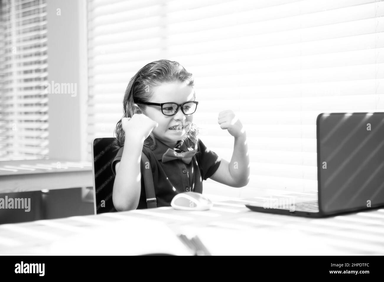 Un écolier enthousiaste utilisant un ordinateur portable et étudiant la leçon en ligne. Élève à l'école. Enfant mignon utilisant un ordinateur portable, étudiant en ligne. Banque D'Images