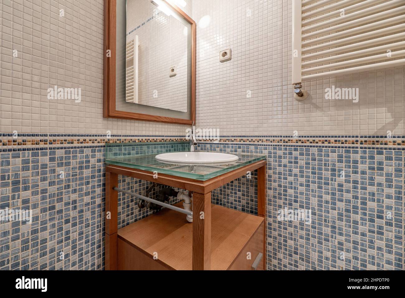 Toilettes avec armoire en merisier avec dessus en verre, radiateur mural, miroir carré et carreaux de mosaïque Banque D'Images