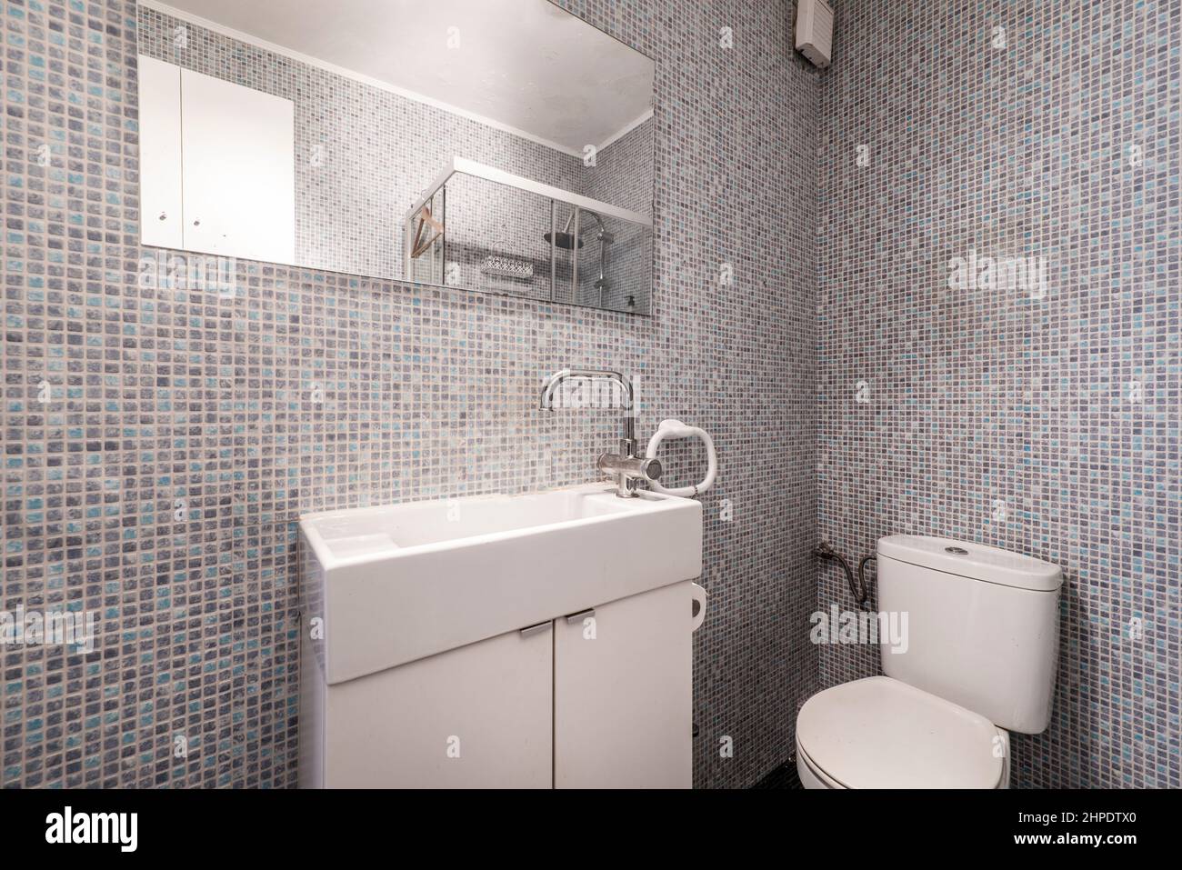 Salle de bains avec évier en porcelaine blanche, miroir mural rectangulaire et carreaux de mosaïque gris et bleu Banque D'Images