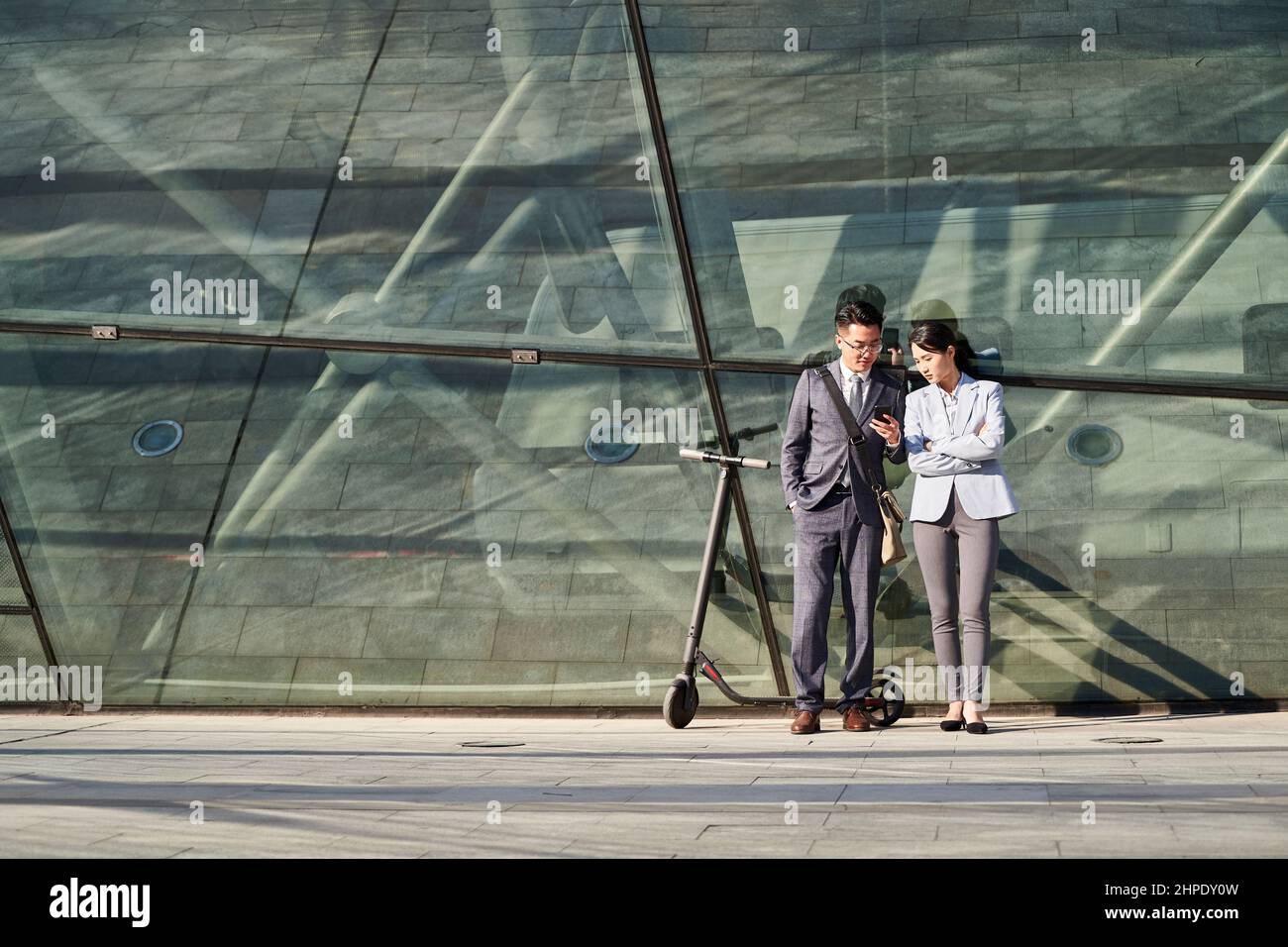 jeune homme d'affaires asiatique et femme debout à l'extérieur regardant le téléphone mobile ensemble Banque D'Images