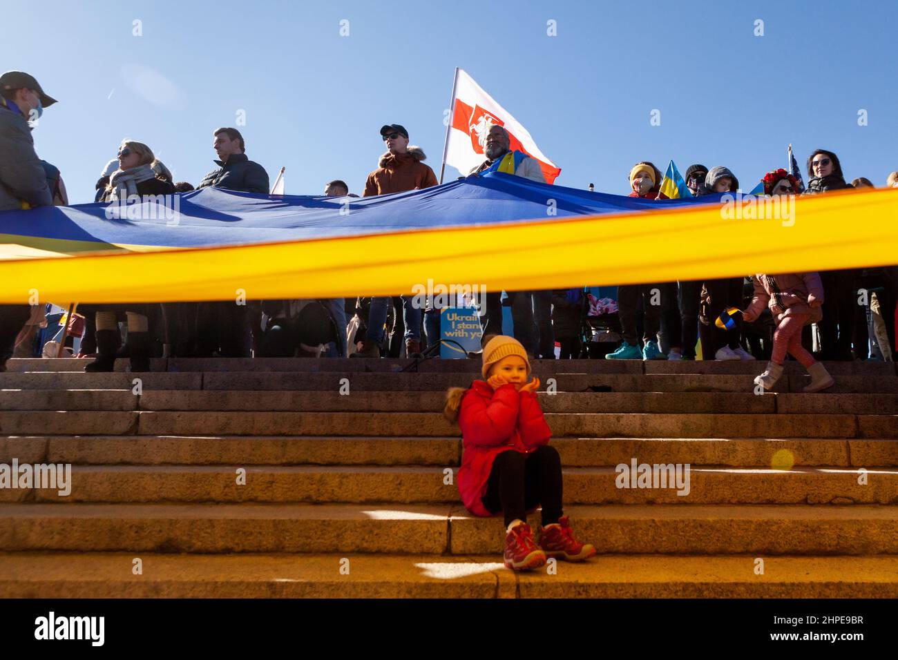 Washington, DC, États-Unis, 20 février 2022. Photo : une jeune fille est assise sous un énorme drapeau lors d'un rassemblement de solidarité pour l'Ukraine. Des milliers de personnes ont assisté à l'événement en faveur de l'indépendance, de la souveraineté et de l'intégrité territoriale de l'Ukraine, alors que le président russe Vladimir Poutine menace l'invasion avec des troupes mobilisées à la frontière. L'événement a été parrainé par Razom, une organisation ukrainienne de plaidoyer, et a inclus une vigile pour les cent Heavenly / Nebesna sotnia (ceux tués pendant la révolution de la dignité de 2014), ainsi qu'une marche à la Maison Blanche. Crédit : Allison Bailey / Alamy Live News Banque D'Images